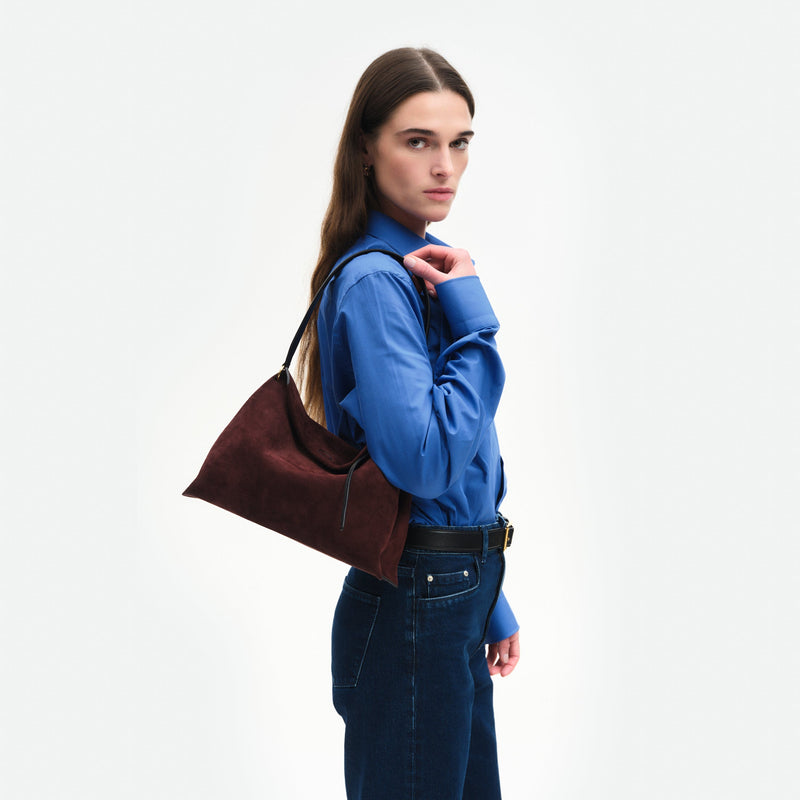 Wandler Penelope Tote Small in the color Acai Suede / Black made from calf leather with golden hardware and soft slouchy silhouette, pictured on model, being worn on the shoulder, half body picture.