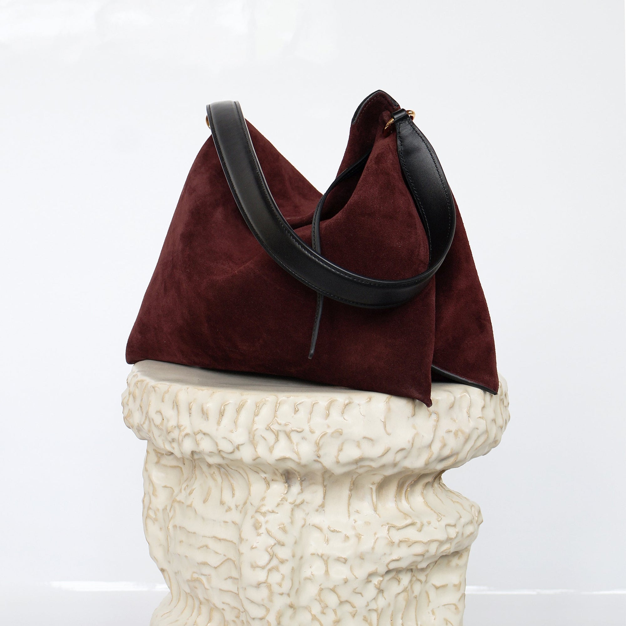 Wandler Penelope Tote Small in the color Acai Suede / Black made from calf leather with golden hardware and soft slouchy silhouette, front view, pictured on pillar.