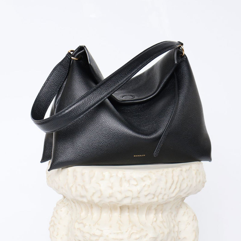 Wandler Penelope Tote Small in the color Black Crust made from calf leather with golden hardware and soft slouchy silhouette, pictured on pillar.