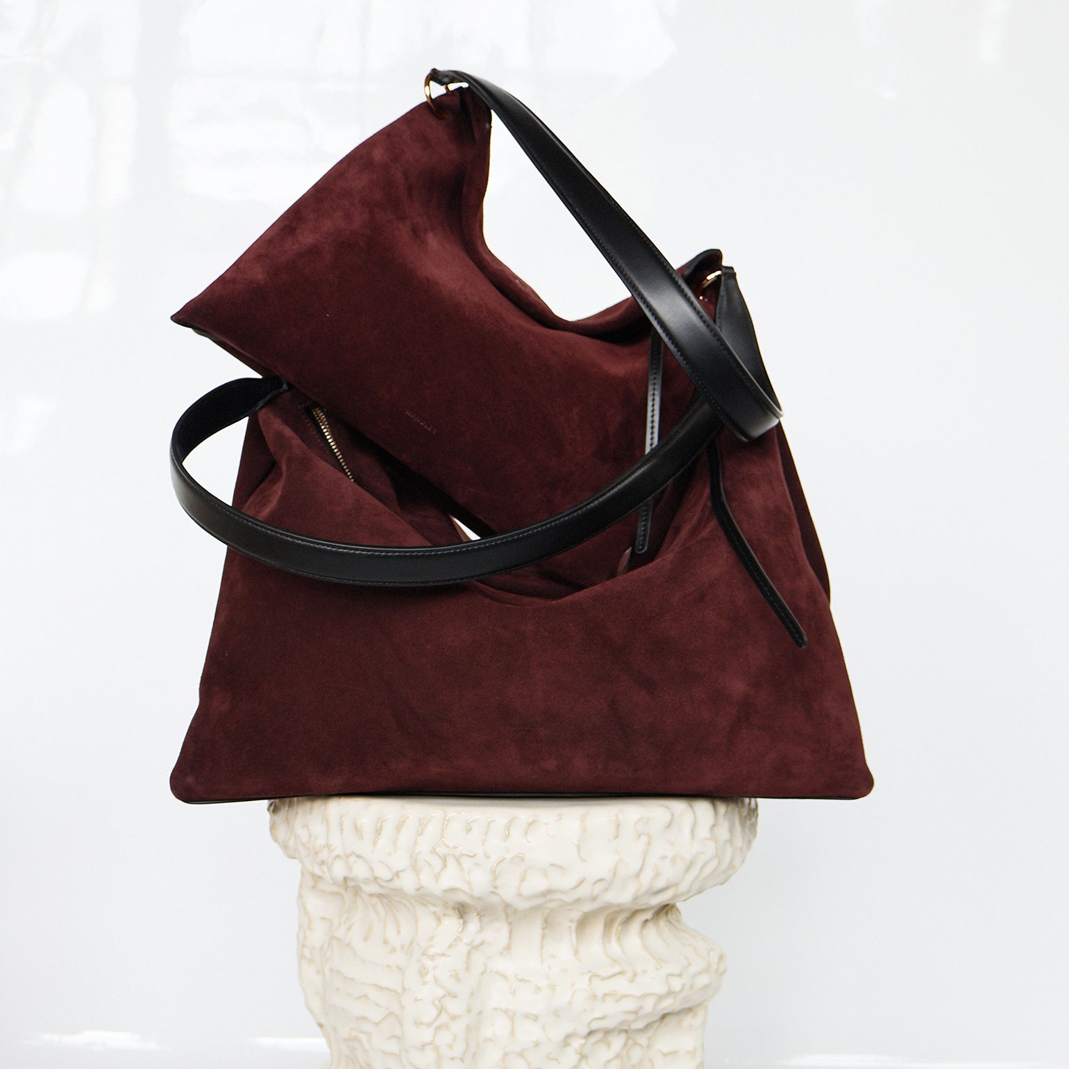 Wandler Penelope Tote Small in the color Acai Suede / Black made from calf leather with golden hardware and soft slouchy silhouette, pictured on pillar together with the regular Penelope Tote Acai Suede / Black to show the difference in size.
